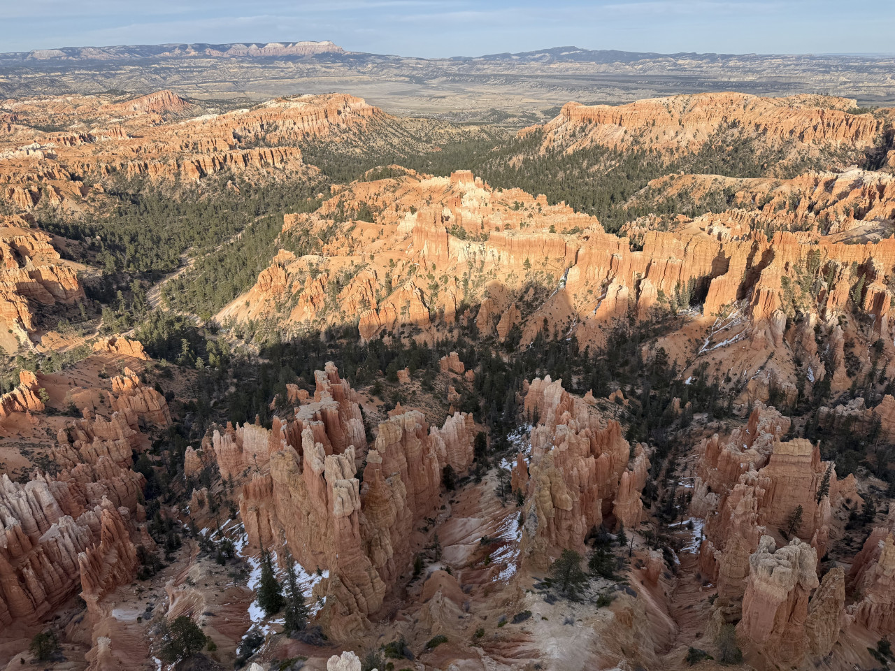 Panorama Bryce Canyonu: oranžové skalní věže hoodoo, borovicové lesy a zbytky sněhu.
