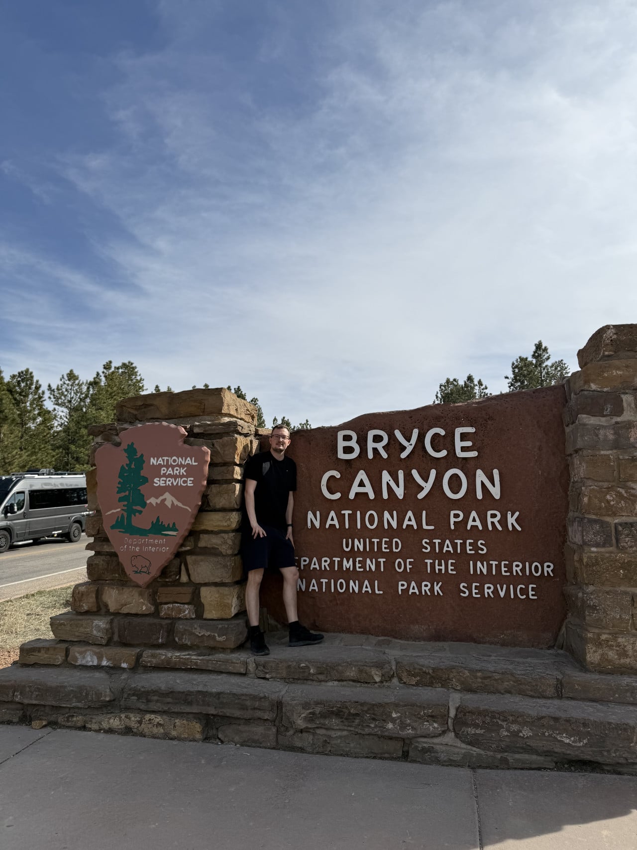 Muž u vstupní cedule BRYCE CANYON NATIONAL PARK, logo National Park Service