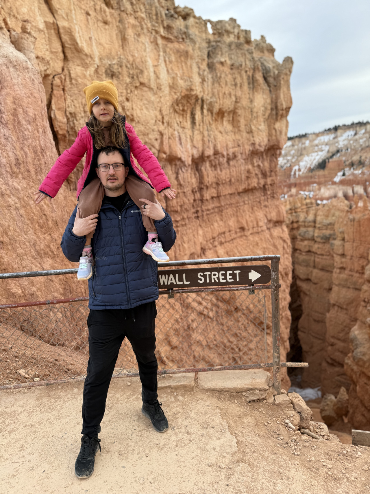Muž nese dívku na ramenou u cedule WALL STREET →, Bryce Canyon