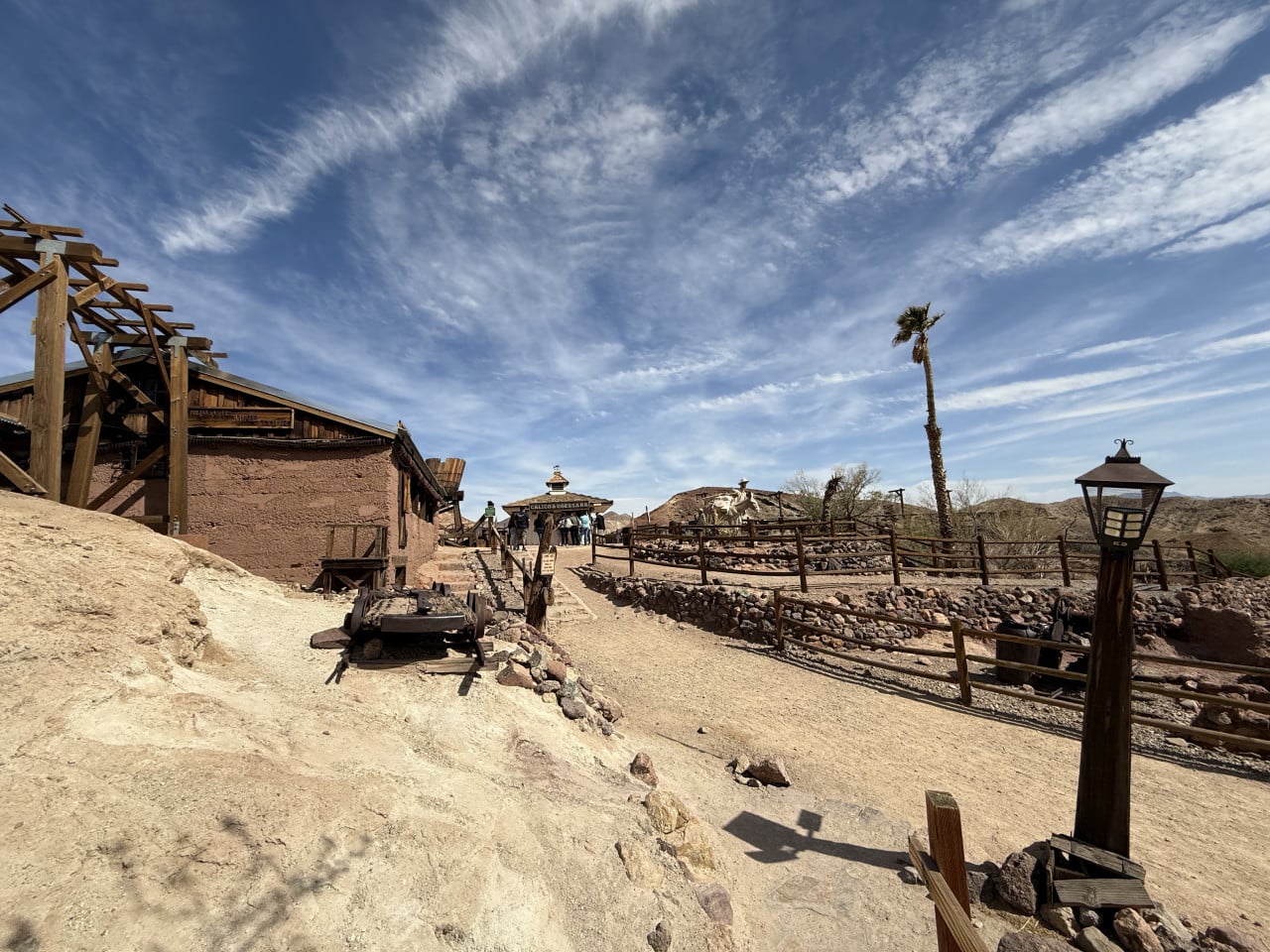 Pouštní cesta v Calico Ghost Town s dřevěnými budovami, palmou a nápisem Calico Odessa Bar.