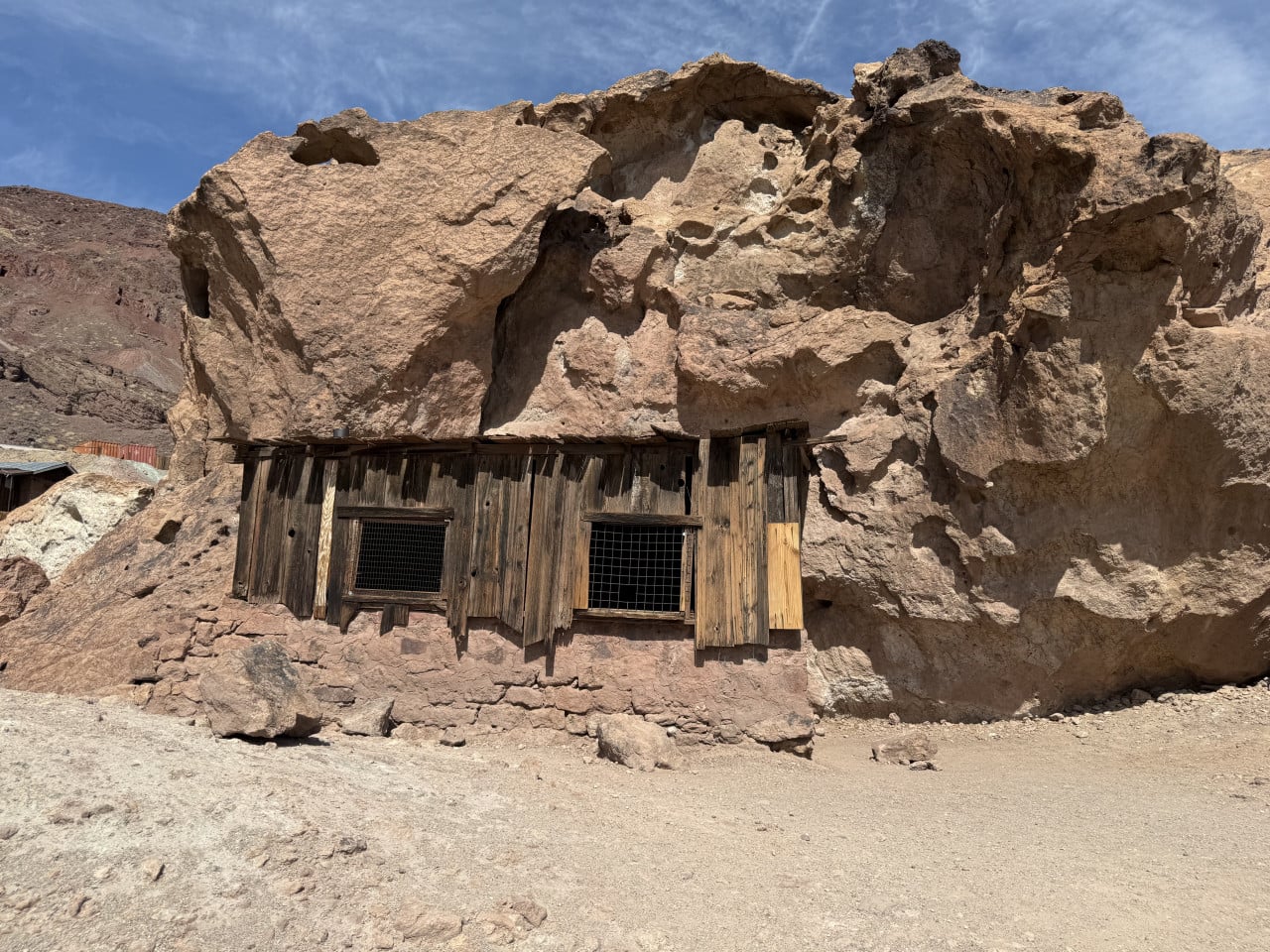 Dřevěná chatka zabudovaná do skalní stěny v poušti pod modrou oblohou