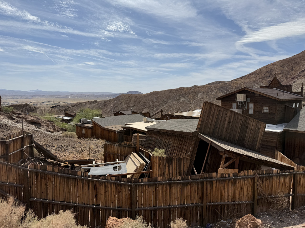 Dřevěné budovy Calico Ghost Town v poušti, s dřevěným plotem a horami v pozadí