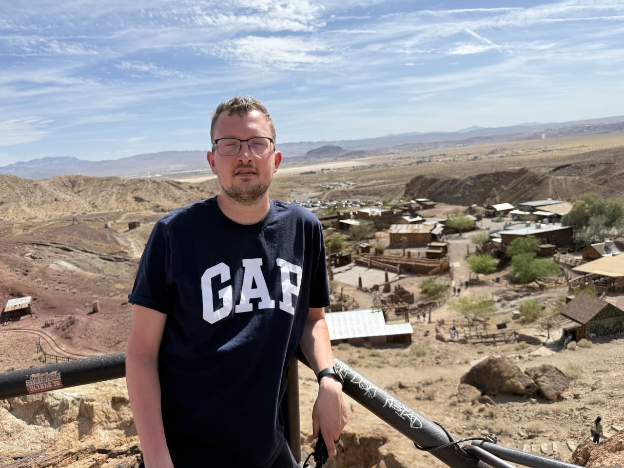 Muž v brýlích stojí nad Calico Ghost Town v pouštní krajině.