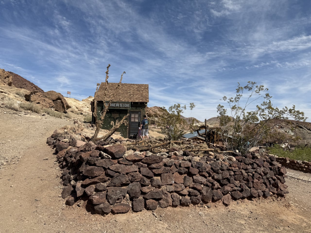Pouštní domek s cedulí WHERSIDE, kamenitá zídka a modrá obloha v Calico Ghost Town