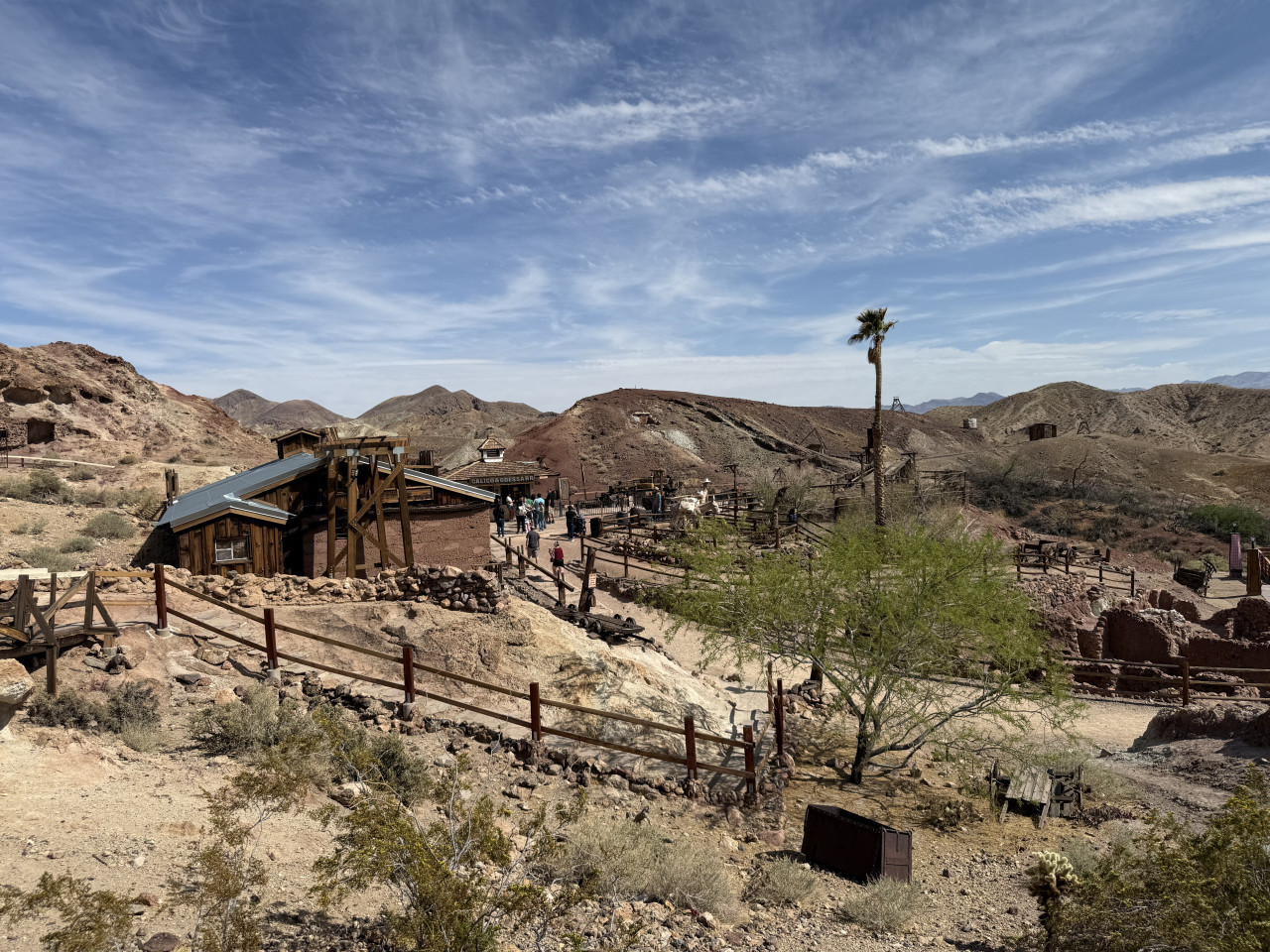 Pohled na Calico Ghost Town v pouštních kopcích s dřevěnými budovami a palmou.