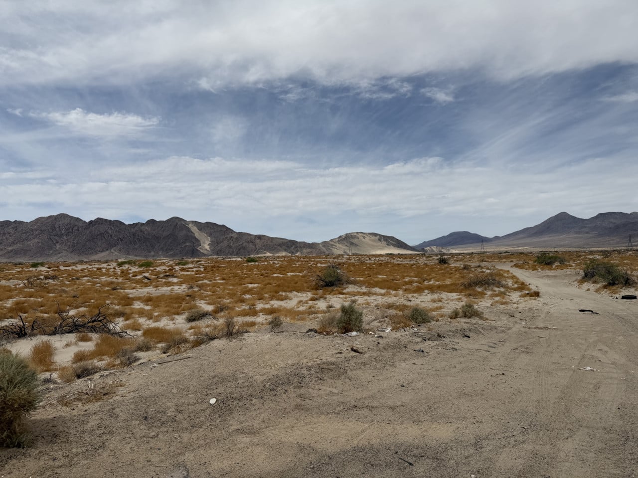 Pouštní krajina Mojave s hnědými keři, horami a oblaky na obloze