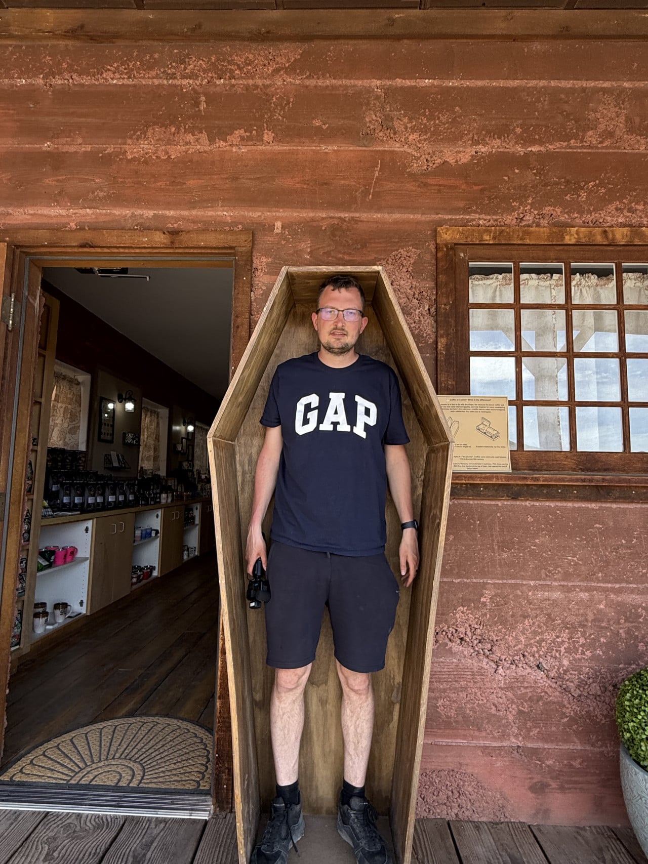 Muž stojí v dřevěné rakvi před vchodem do starého domu.