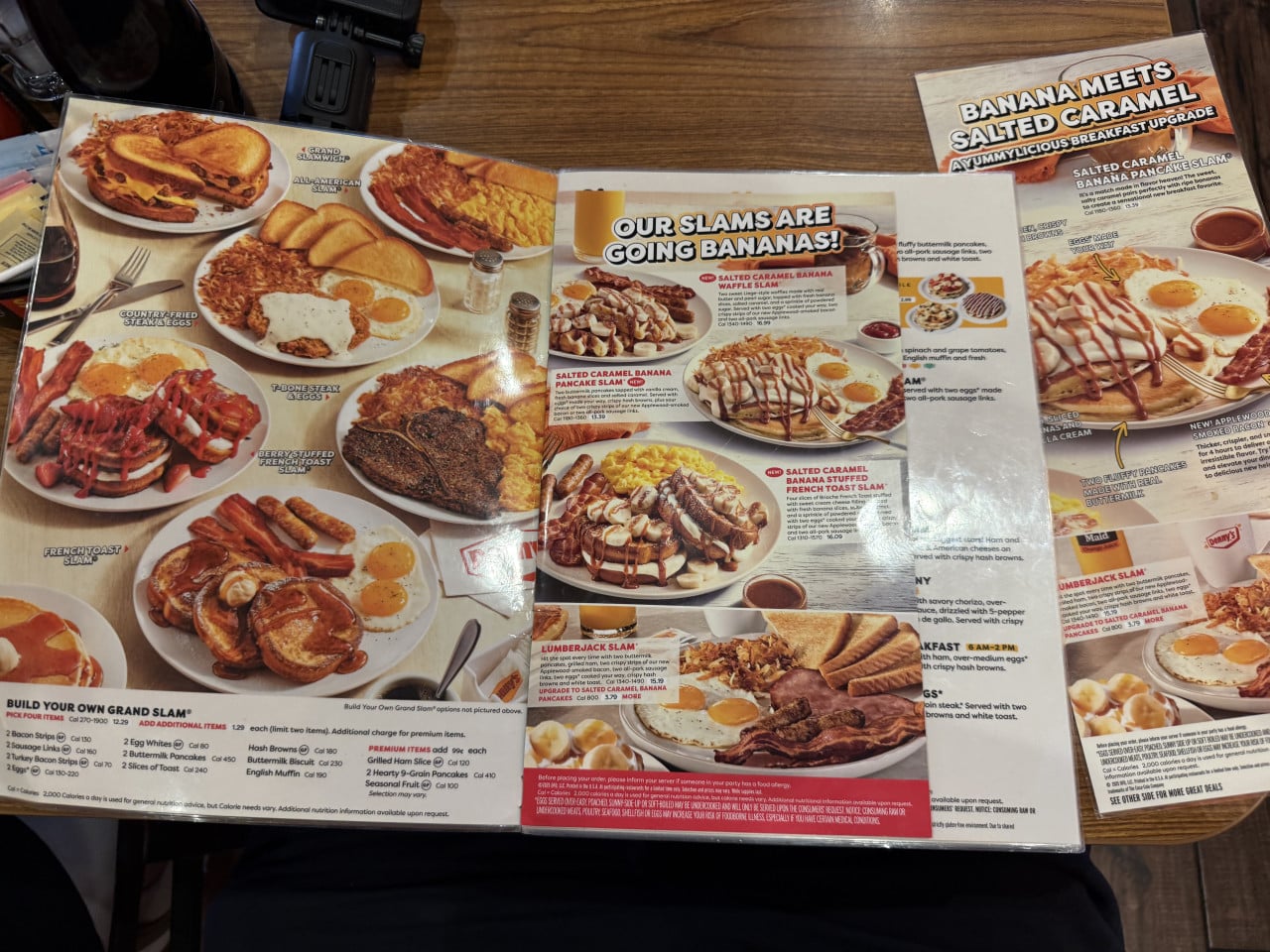 Otevřené menu Denny’s se snídaňovými jídly na dřevěném stole.