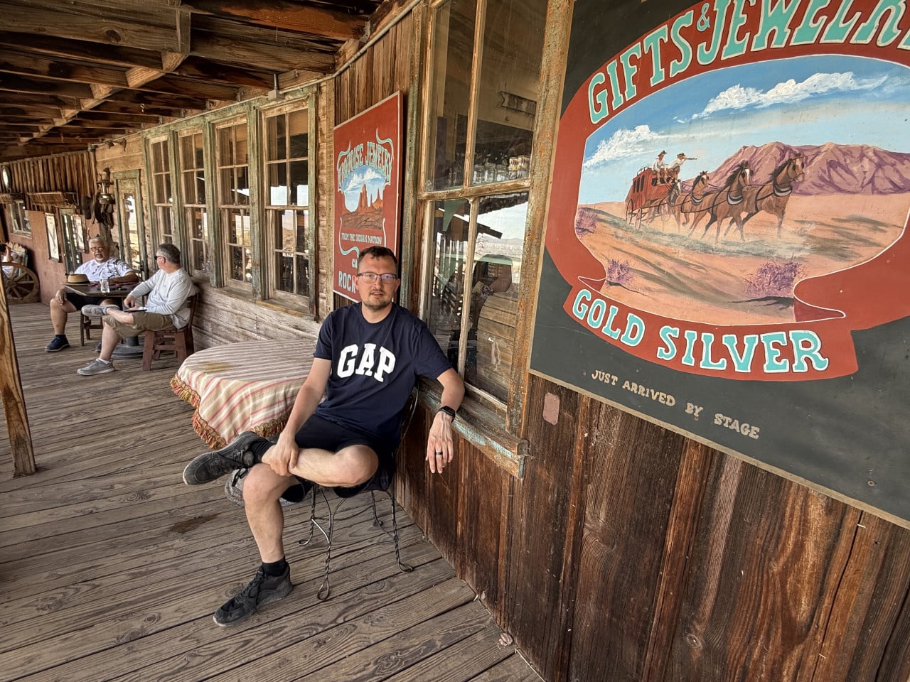 Muž sedí na dřevěné verandě u westernových plakátů v Calico Ghost Town.