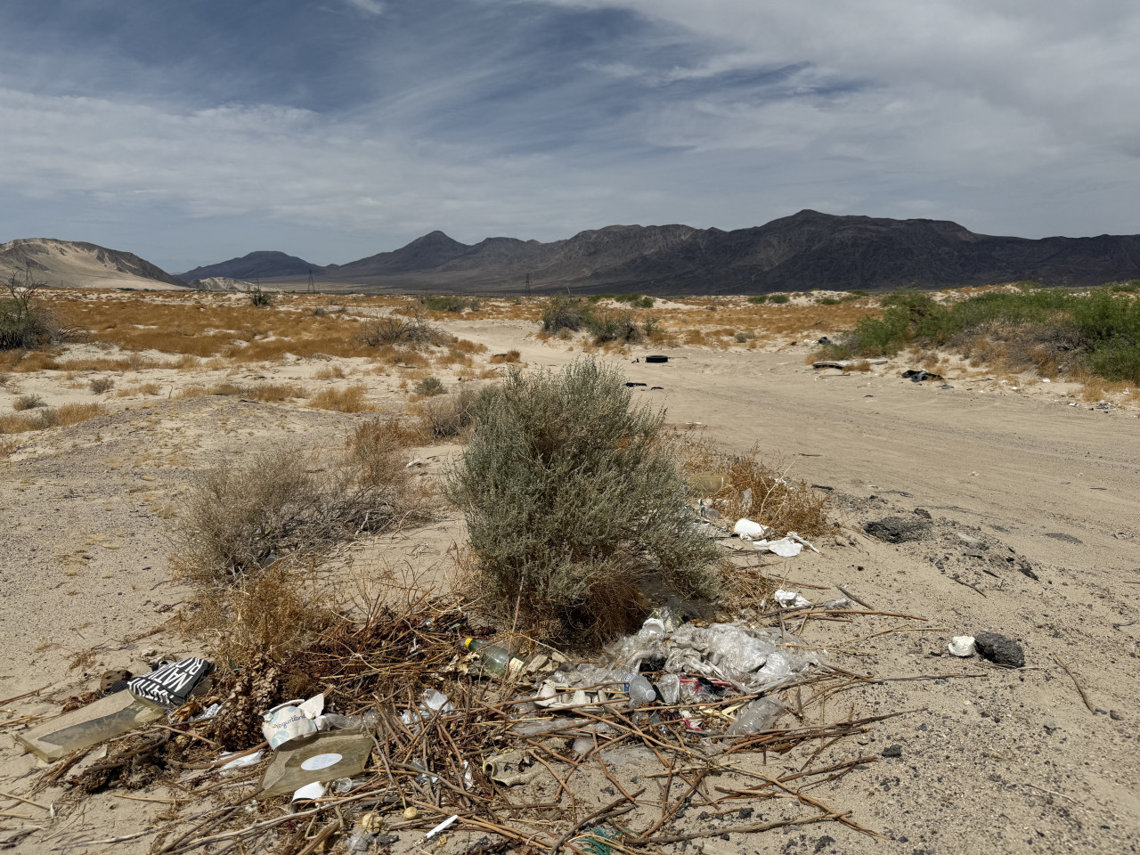 Odpadky v písčité poušti pod horským hřebenem a zamračenou oblohou