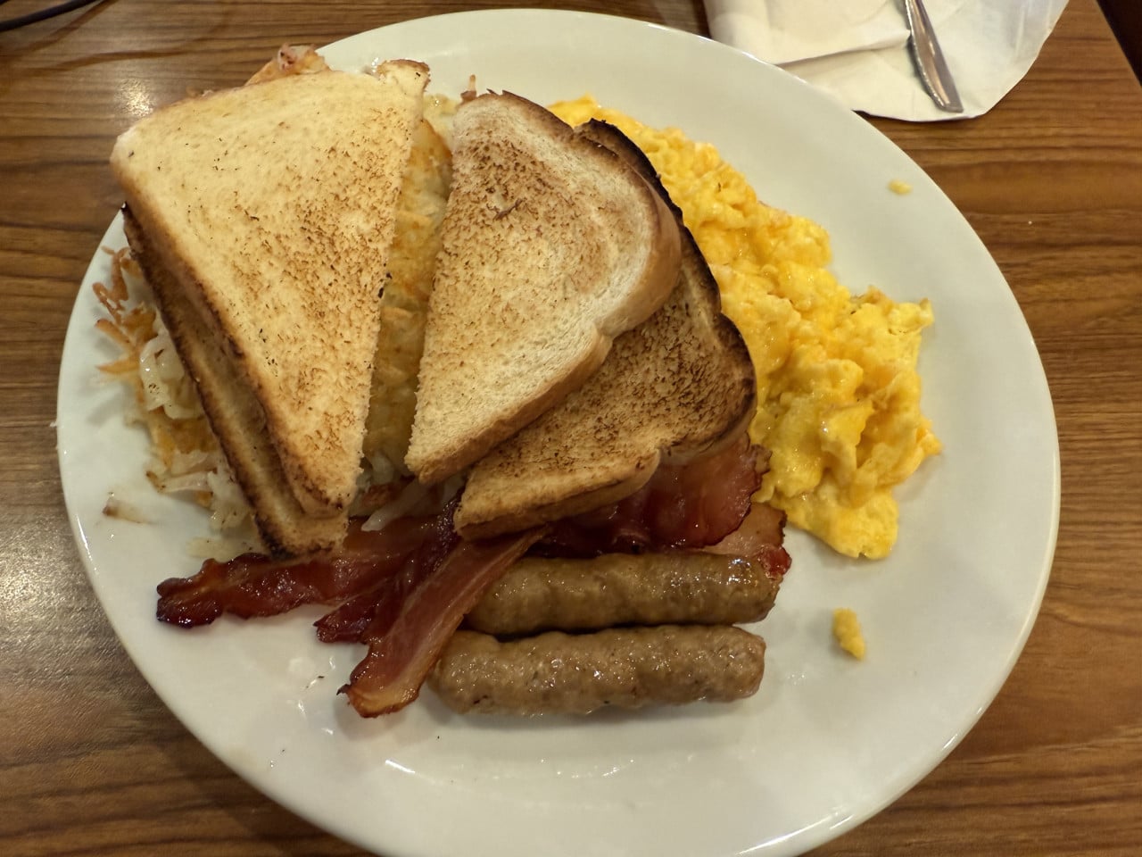 Americká snídaně s tousty, vejci, slaninou, klobásami a hash browns na talíři.