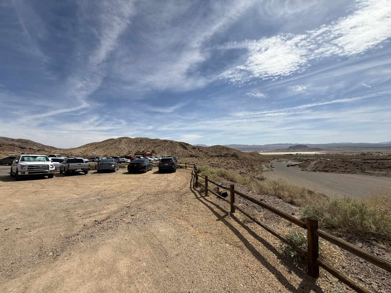 Parkoviště v pouštní krajině s auty, kopci a širokou modrou oblohou