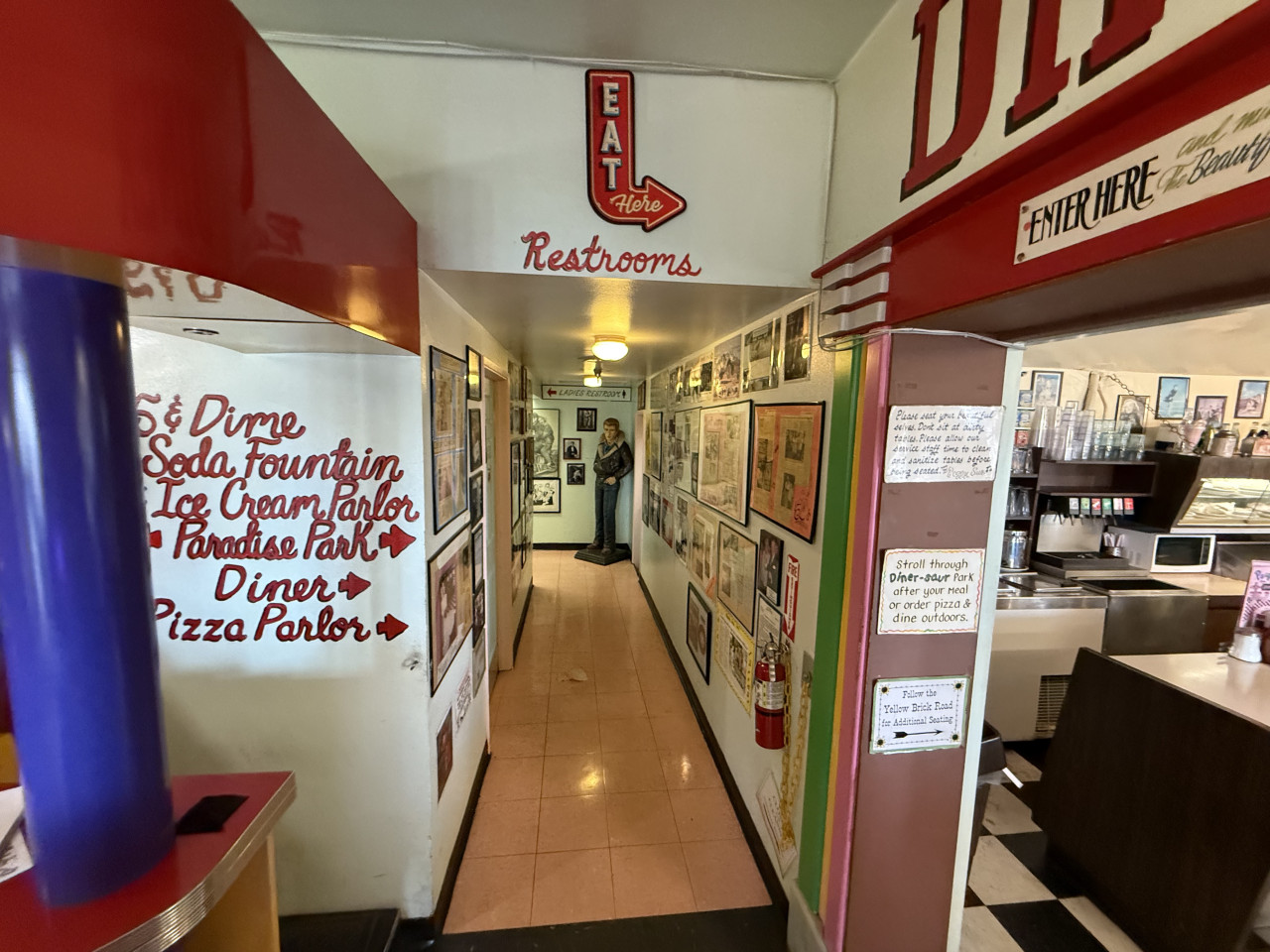 Retro restaurace s úzkou chodbou, nápisem EAT Here a směrovkami k restauracím.