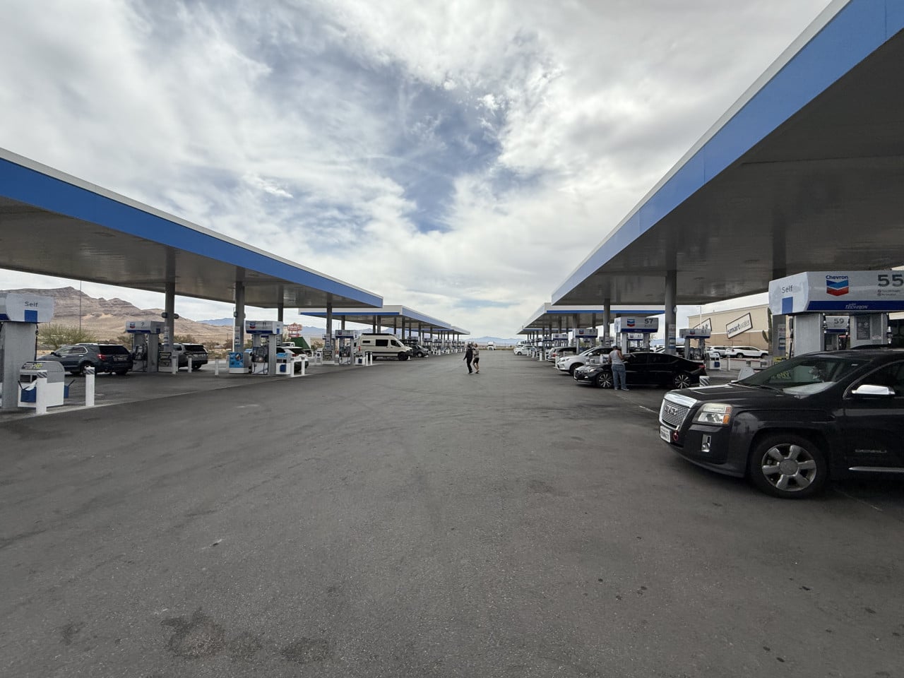Velká chevronová čerpací stanice v poušti s auty a horami v pozadí