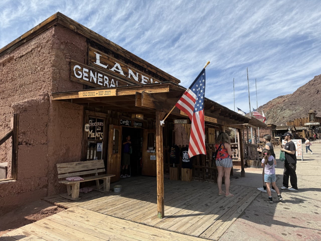 Dřevěný obchod Lane’s General Store v Calico Ghost Town s americkou vlajkou a návštěvníky.