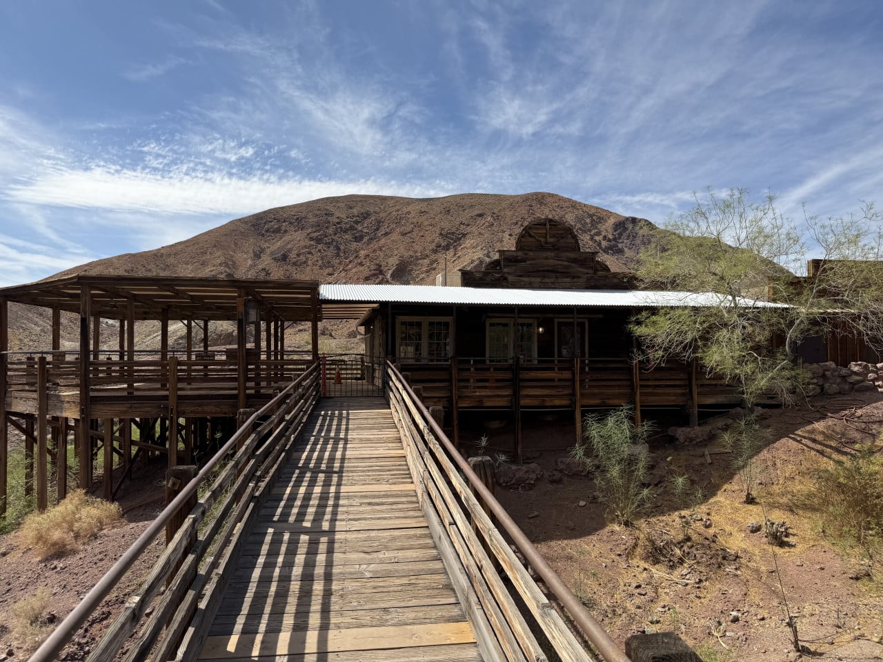 Dřevěná lávka vede k rustikální budově v pouštní krajině Calico Ghost Town.