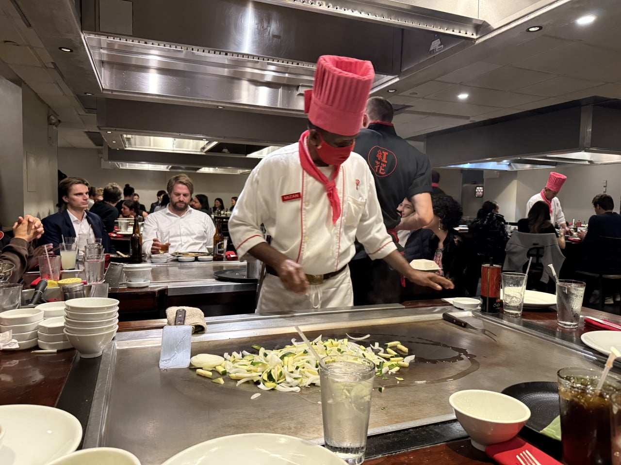 Chef v Benihaně u teppanyaki stolu připravuje jídlo před hosty.