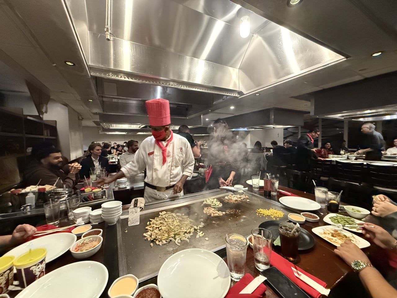 Šéfkuchař v červené čepici vaří u teppanyaki stolu v restauraci Benihana.