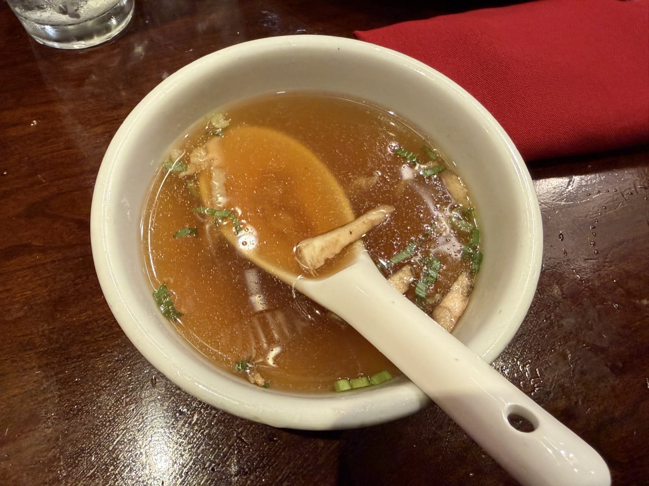 Miska polévky s lžící na dřevěném stole, vedle červený ubrousek.