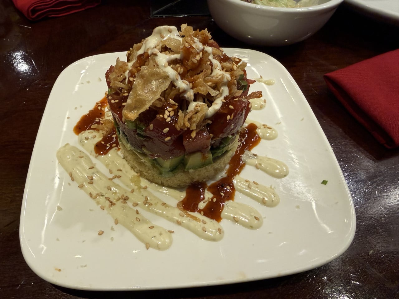 Předkrm z tuňáka, avokáda a omáček na bílém talíři v restauraci.