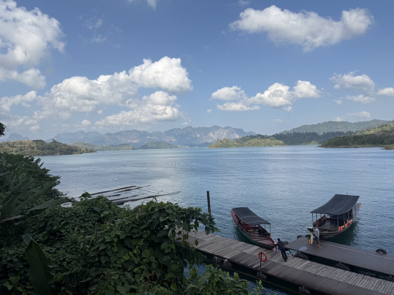 Molo na jezeře Cheow Lan s dvěma čluny, hory a mraky.