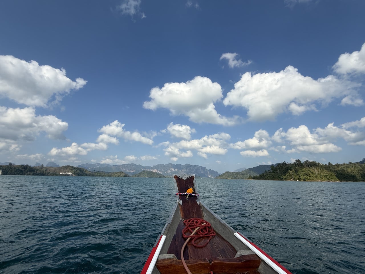 Příď dlouhé lodi na jezeře, v dálce zelené hory a mraky
