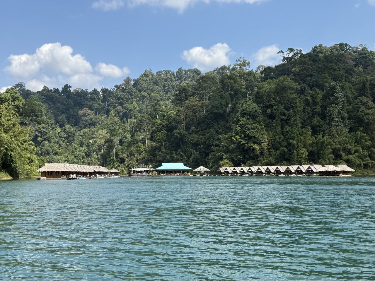 Plovoucí bungalovy na Cheow Lan Lake pod zalesněnými kopci a modrou oblohou