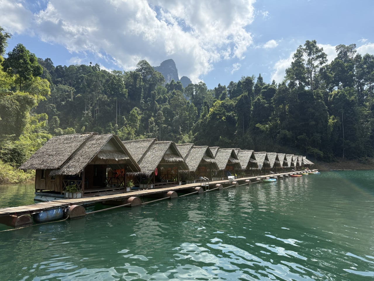 Řada plovoucích bungalovů na smaragdovém jezeře, v pozadí džungle a hory