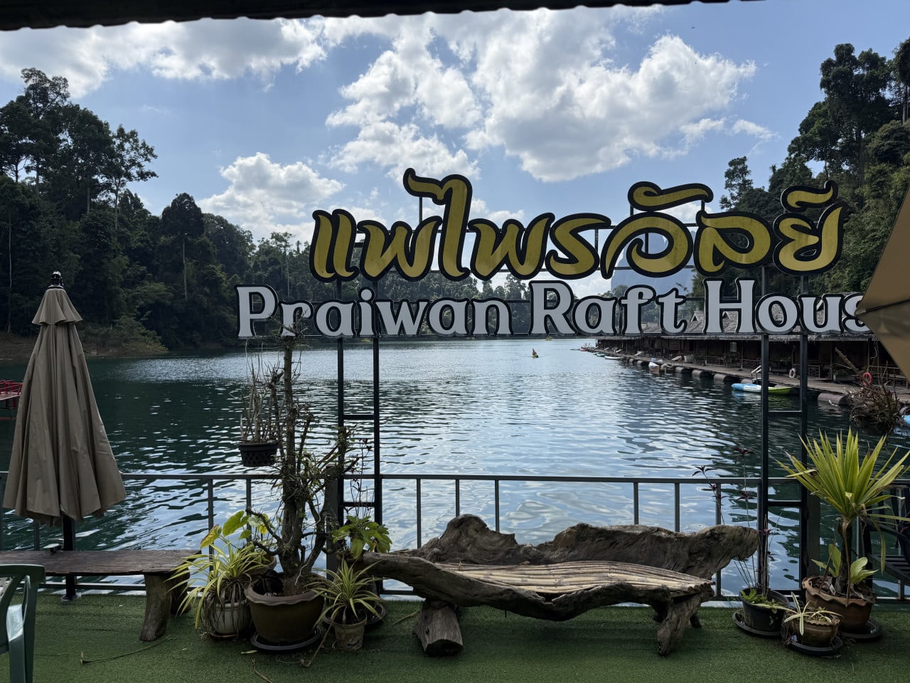 Nápis Praiwarn Raft House a thajské písmo, jezero a plovoucí domky.