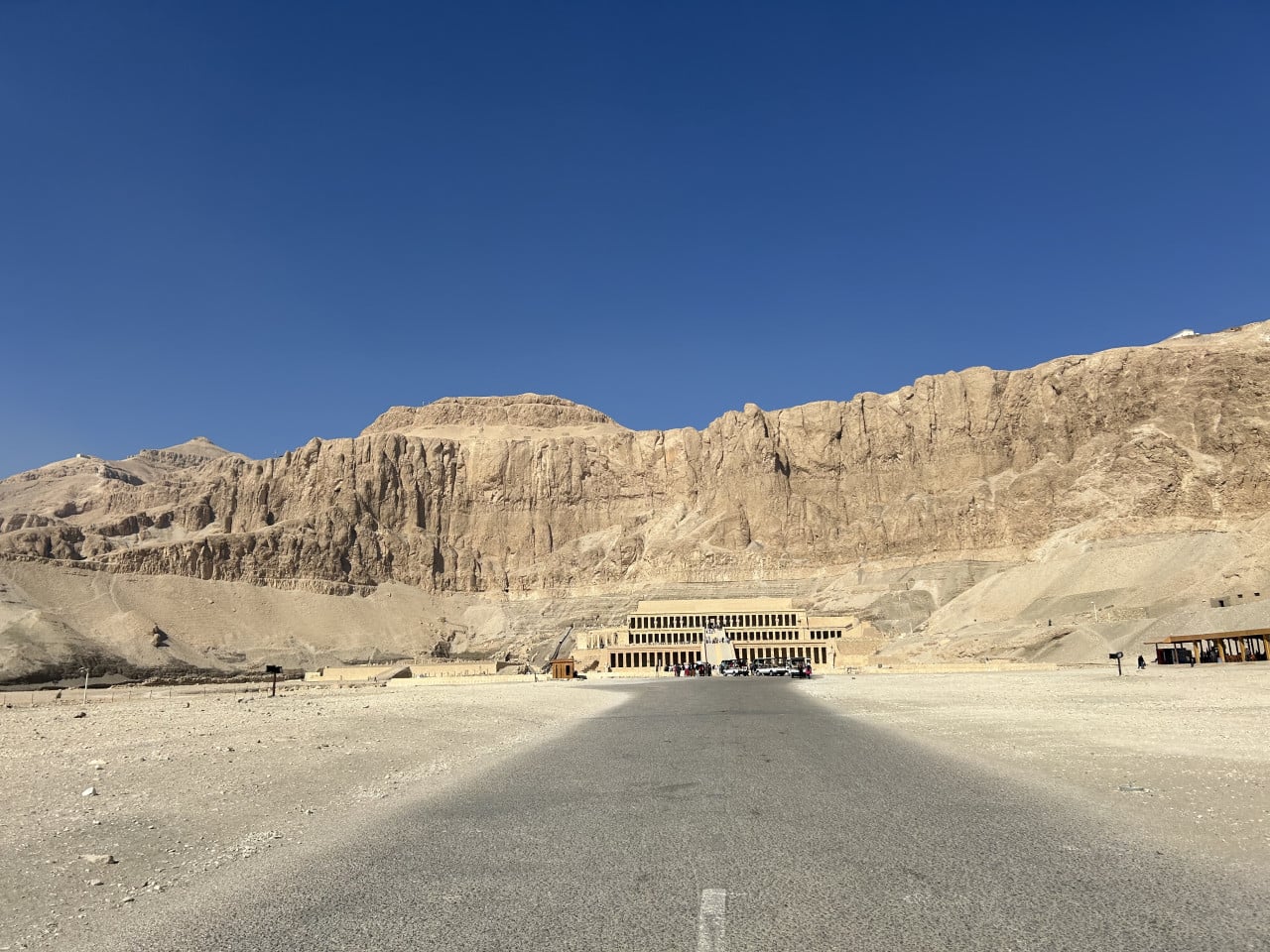 Chrám Hatšepsut pod skalní stěnou v egyptské poušti, široká silnice vpředu.