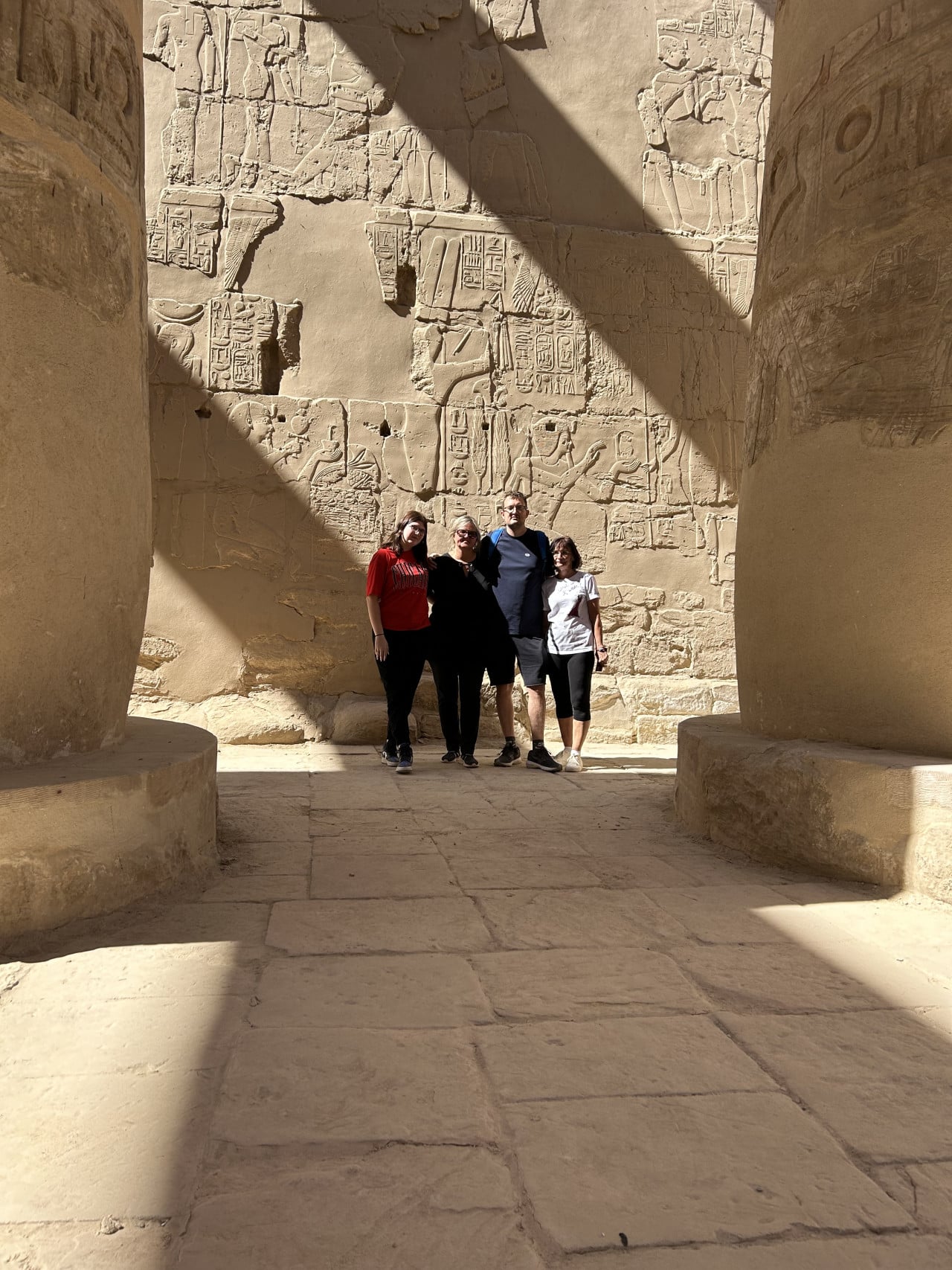 Turisté stojí mezi obřími sloupy a reliéfy v chrámu Karnak.