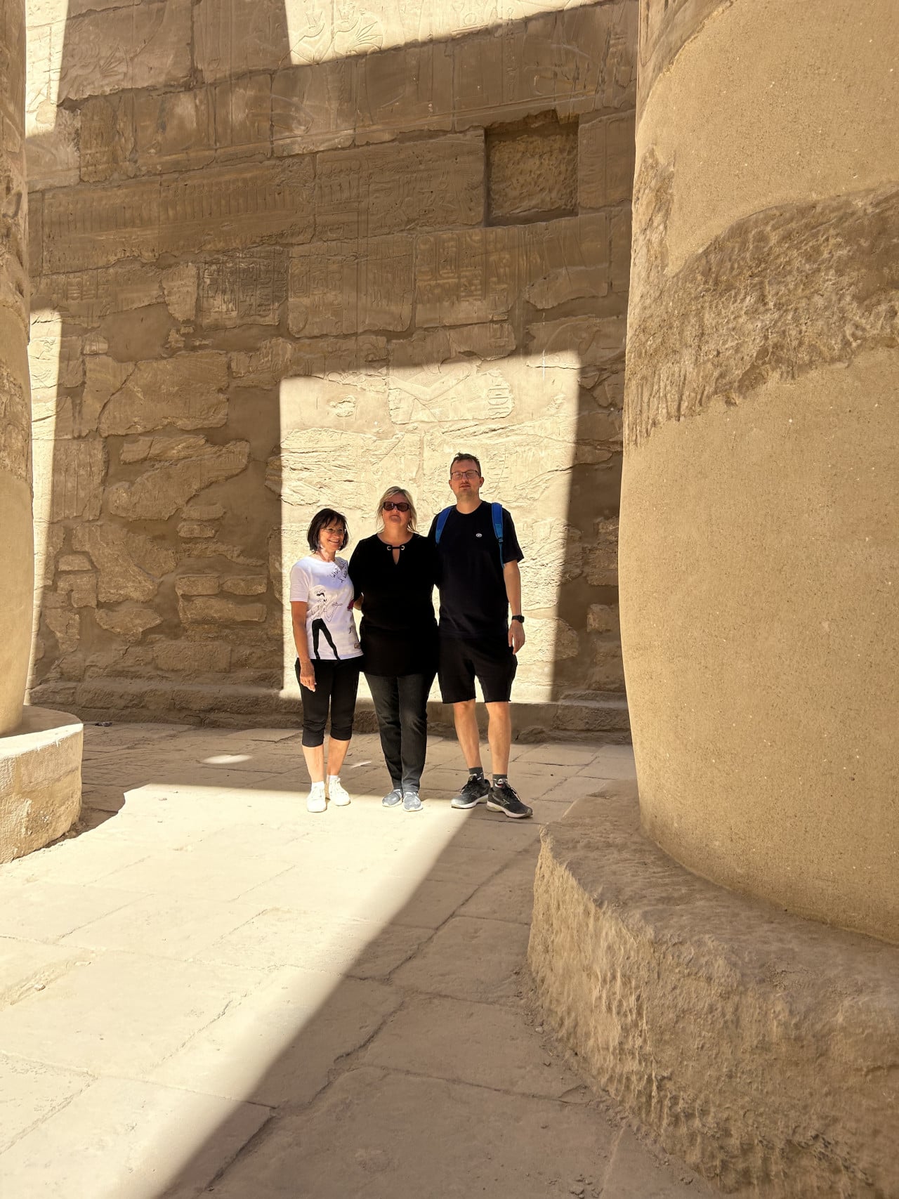 Tři turisté mezi obřími kamennými sloupy v chrámu Karnak