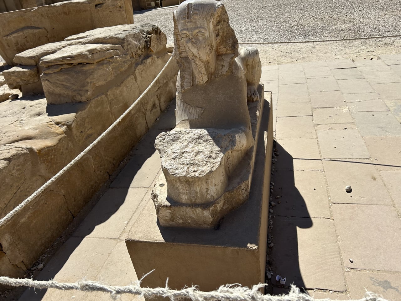 Poškozená kamenná socha sfingy v chrámu Karnak, ohraničená provazem.