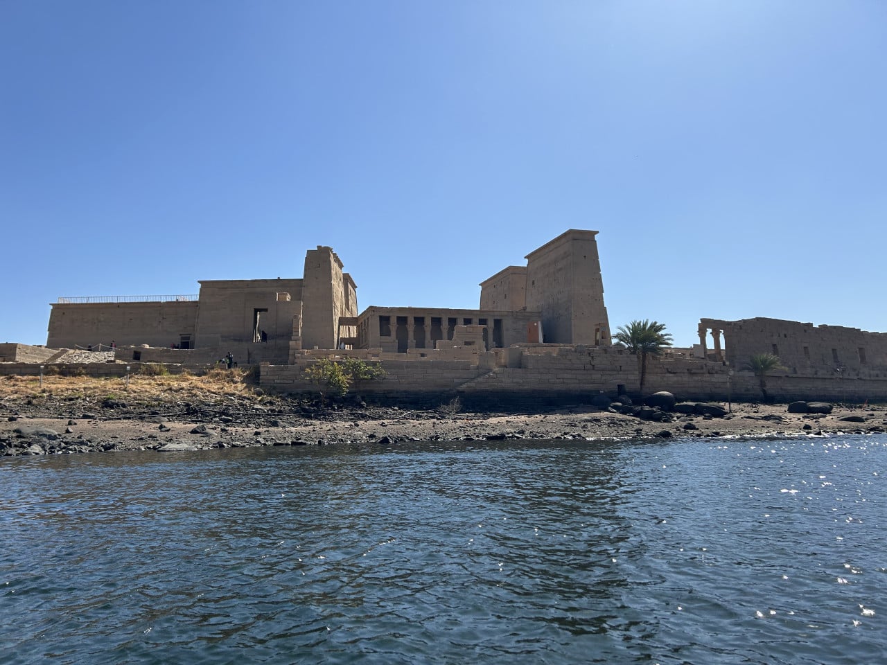 Chrámový komplex Philae na ostrově, pohled z vody pod modrou oblohou