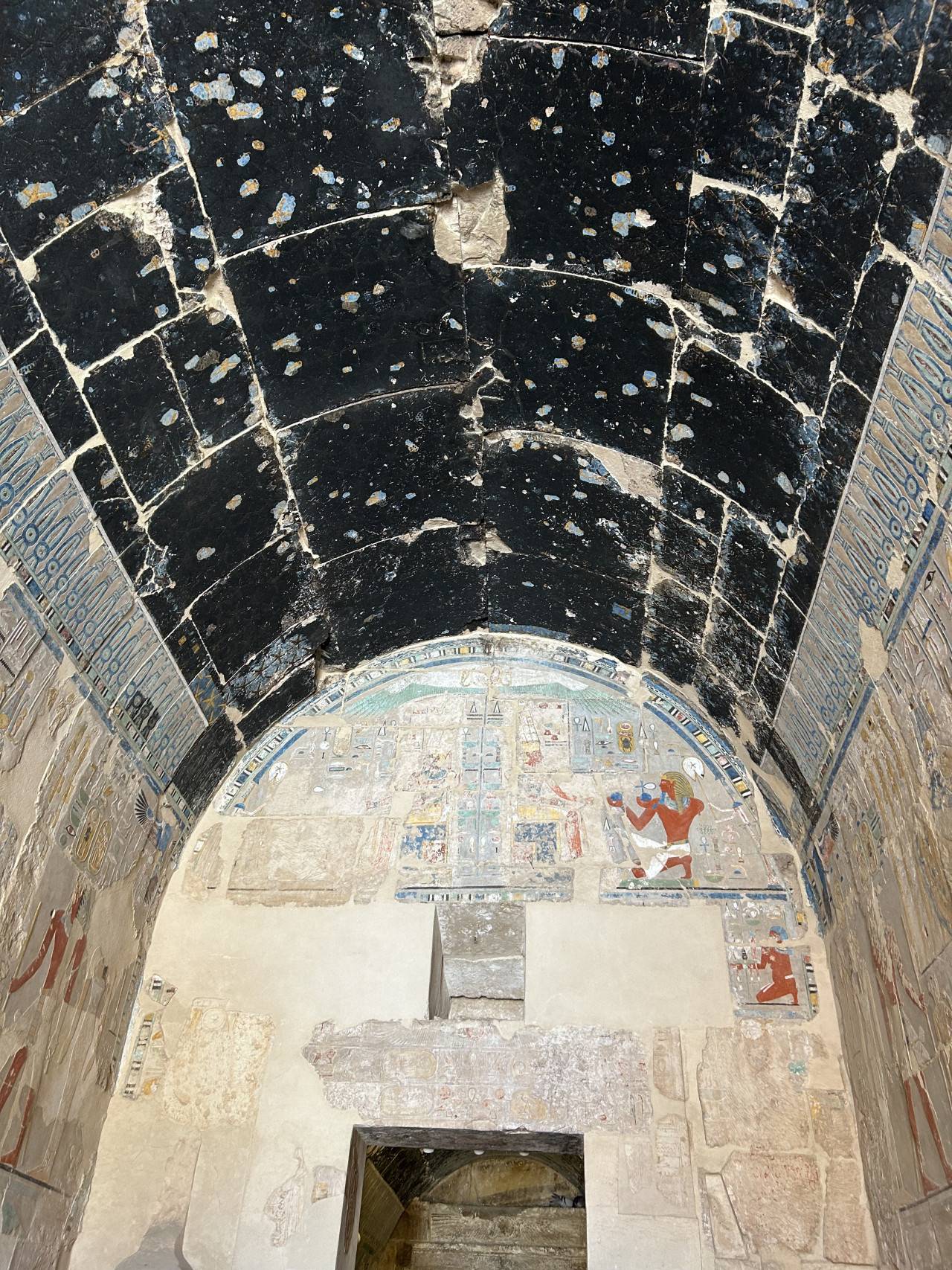 Malovaná chodba s popraskaným černým stropem a hieroglyfy na stěnách egypstkého chrámu