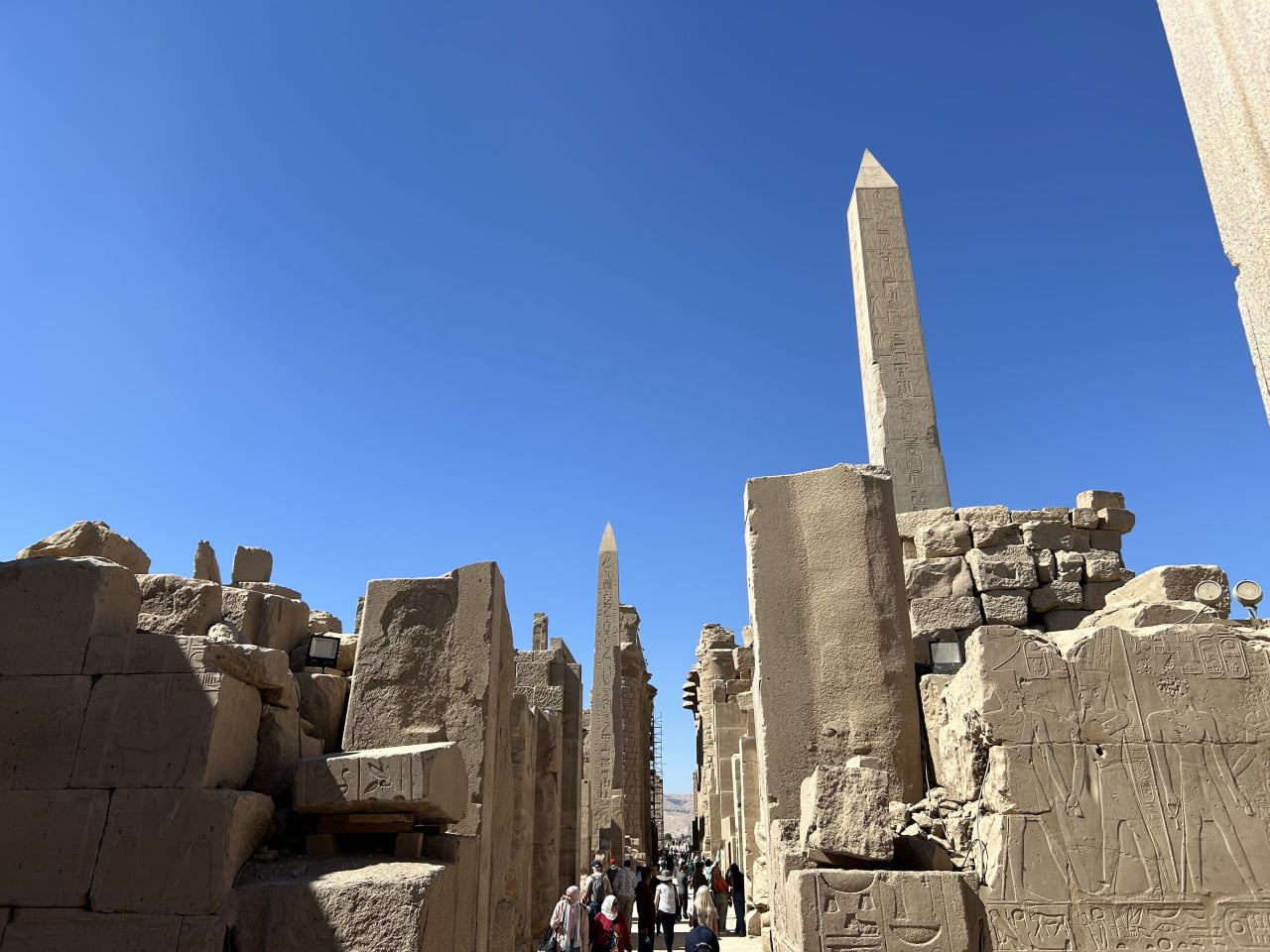 Obelisky a hieroglyfické ruiny chrámu Karnak, turisté na cestě mezi sloupy