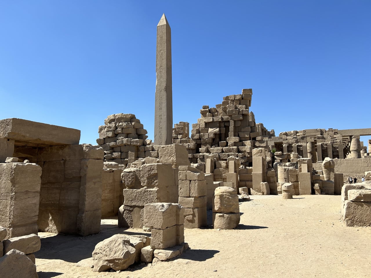 Obelisk, rozvaliny kamenného chrámu a sloupy v Karnaku pod modrou oblohou