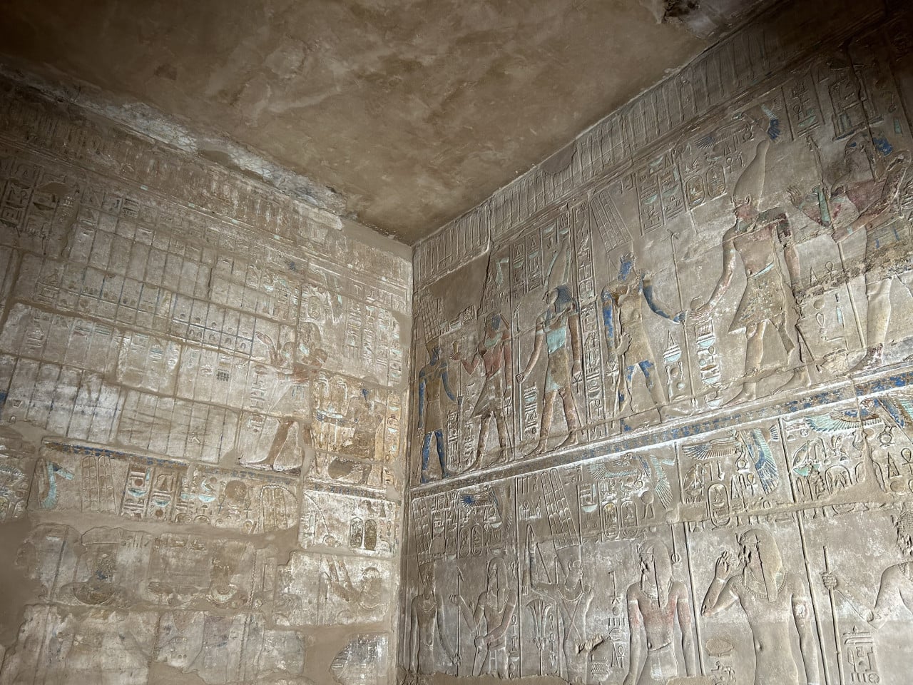 Reliéfní egyptské hieroglyfy a barevné postavy bohů na chrámové stěně.