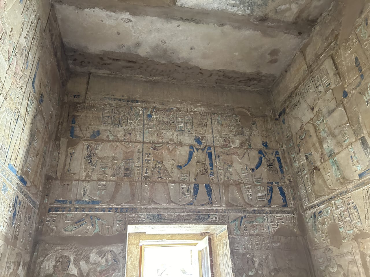 Vyzdobená egyptská komora s hieroglyfy a modrými postavami nad dveřmi