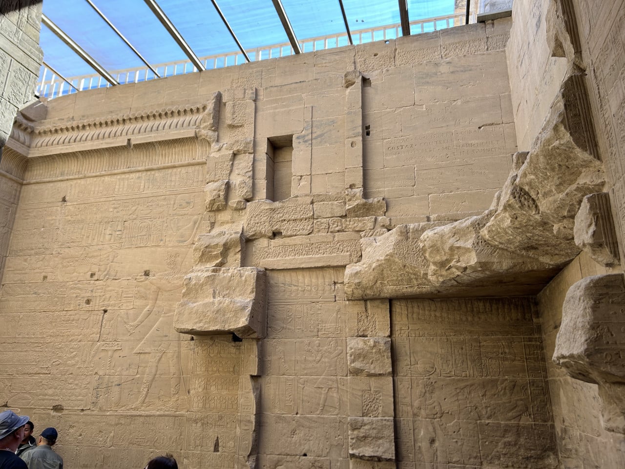 Kamenná stěna Nedokončeného obelisku s hieroglyfy a návštěvníky dole.