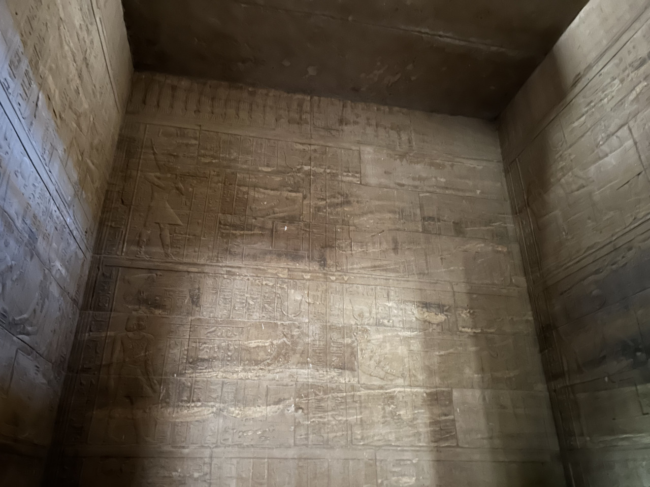 Kamenná stěna egyptského chrámu s vytesanými hieroglyfy a reliéfy.