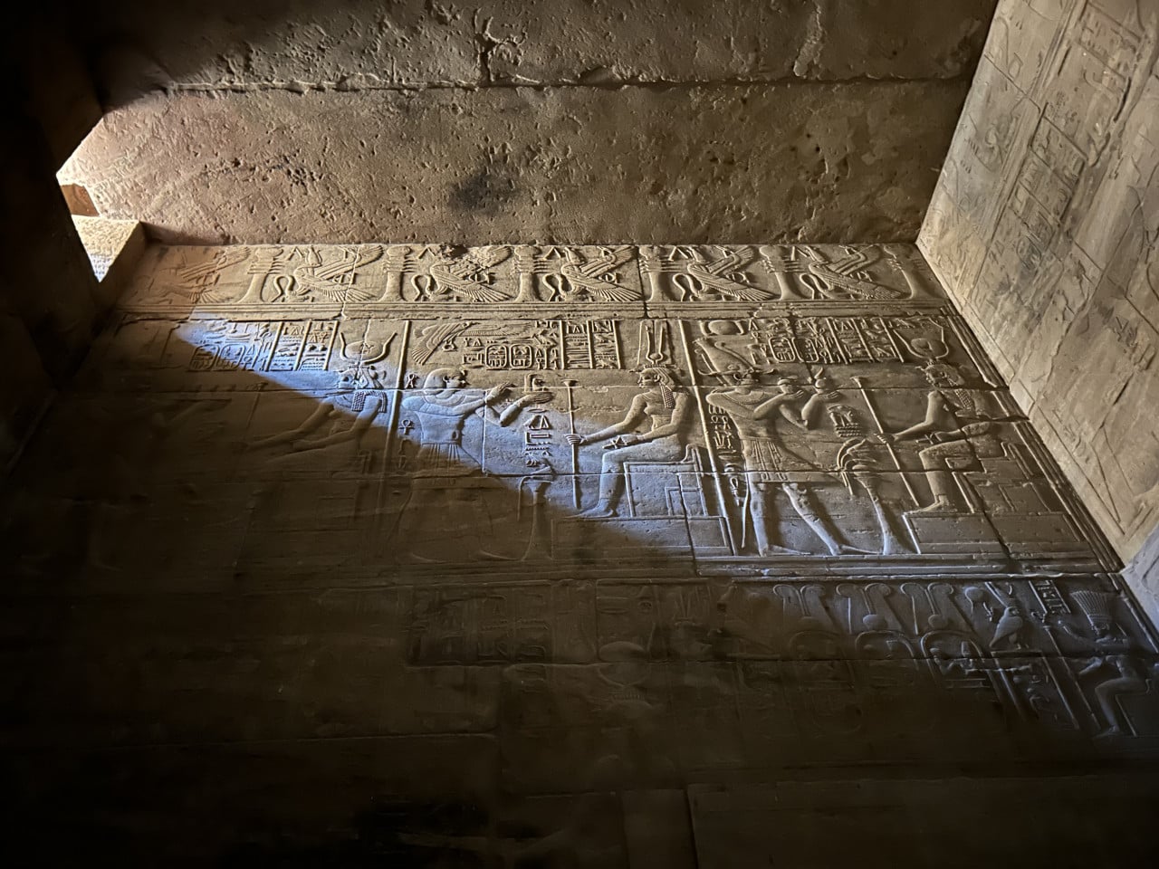 Reliéf egyptských bohů a hieroglyfů osvětlený paprskem světla v chrámu Philae