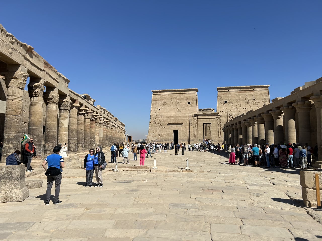 Turisté mezi sloupovím a zdmi chrámu Philae v Asuánu pod modrou oblohou