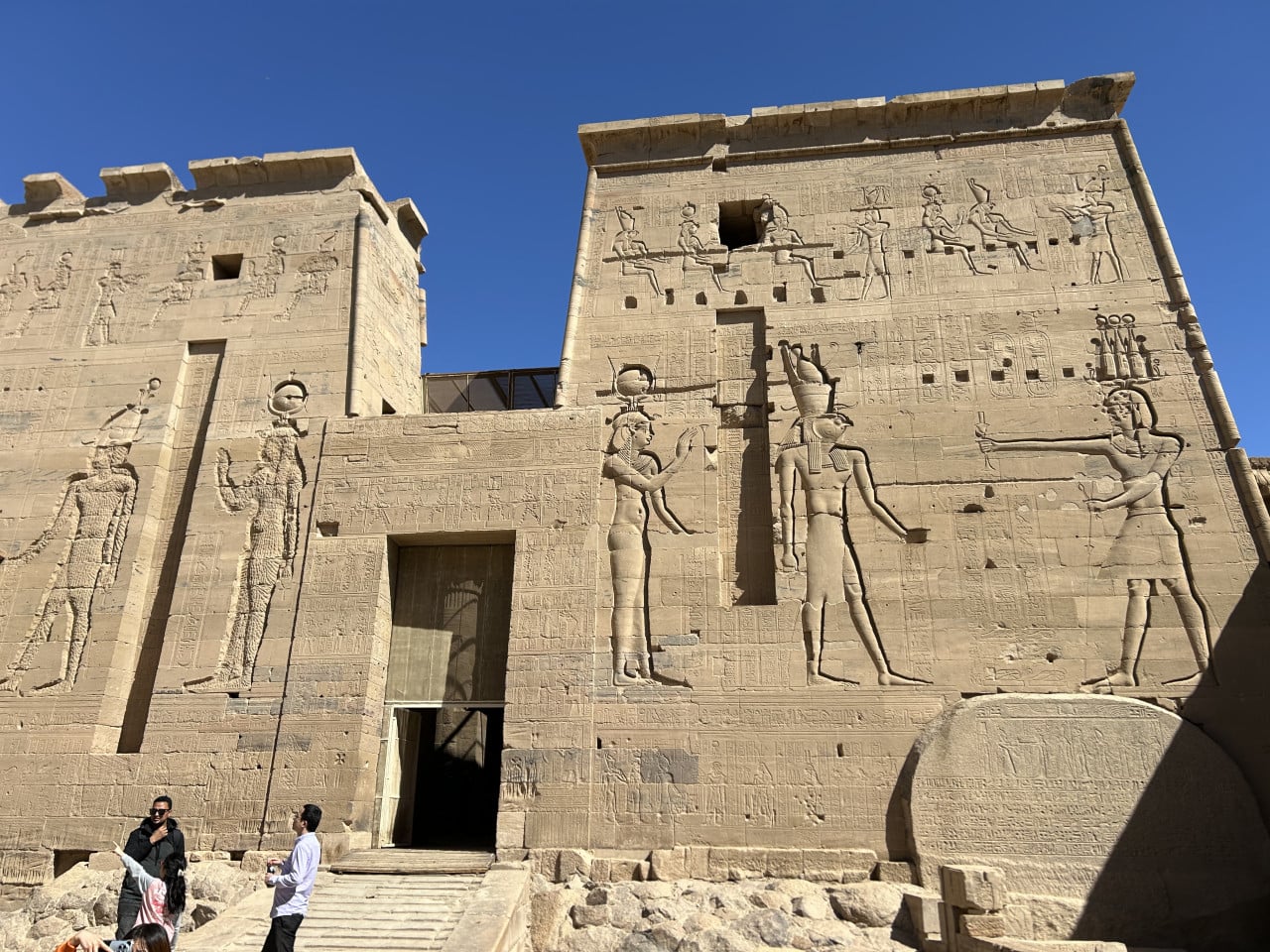 Egyptský chrám Philae s reliéfy bohů a návštěvníky u vchodu