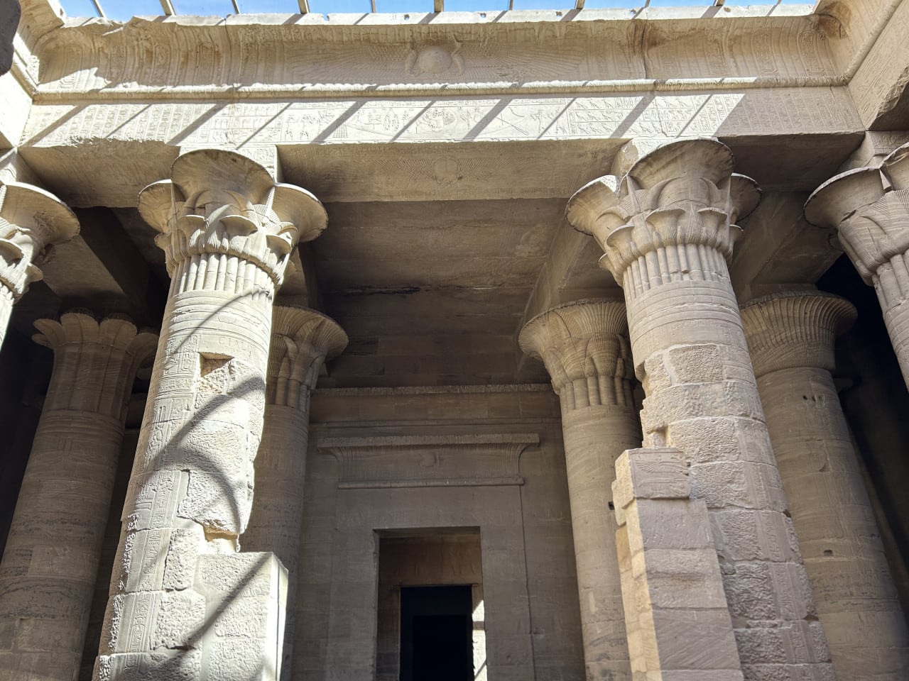 Vnitřek egyptského chrámu s kamennými sloupy a hieroglyfy ve slunečním světle