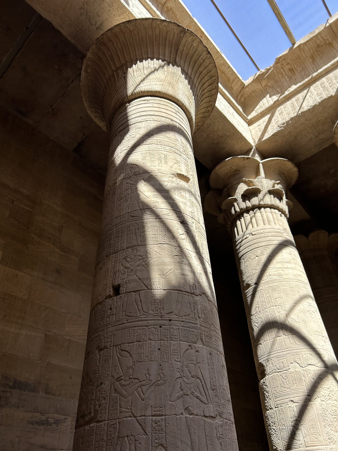 Vyřezávané sloupy chrámu Philae s egyptskými hieroglyfy a slunečními paprsky.