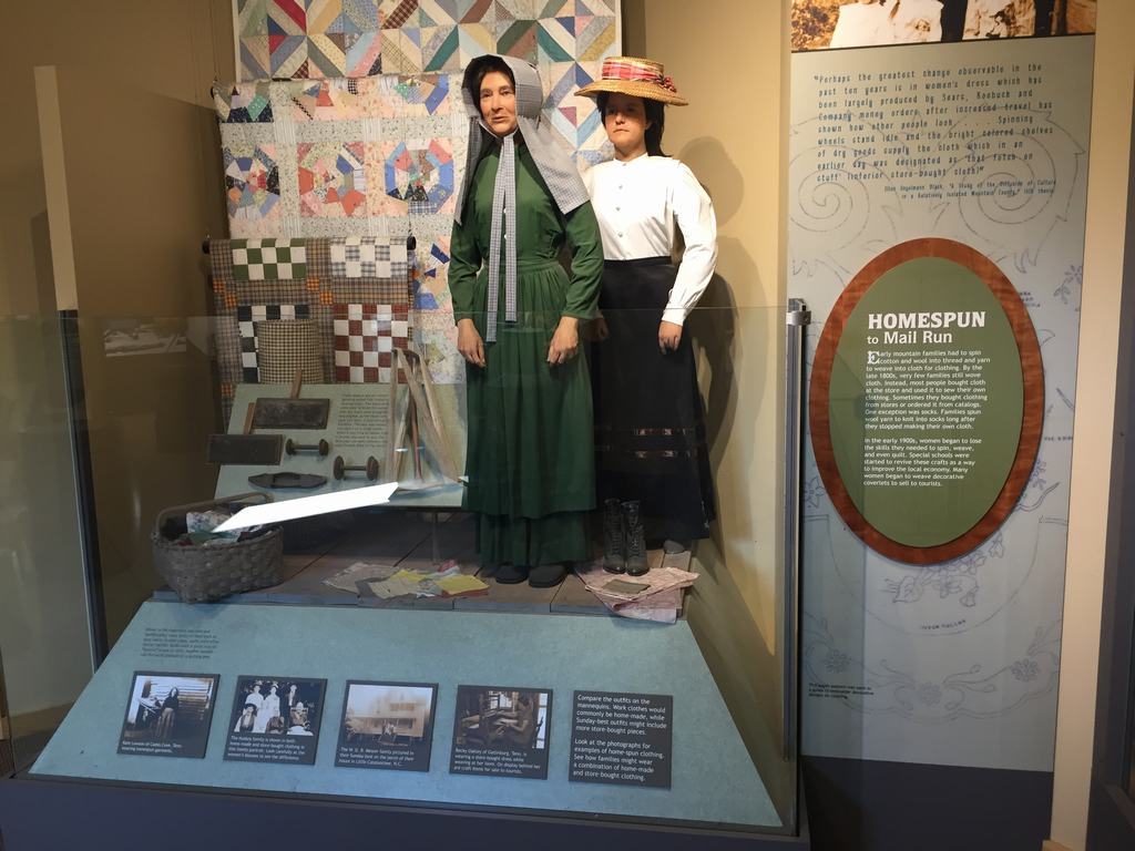 Muzejní vitrína s figurínami v dobových šatech, cedule HOMESPUN to Mail Run.