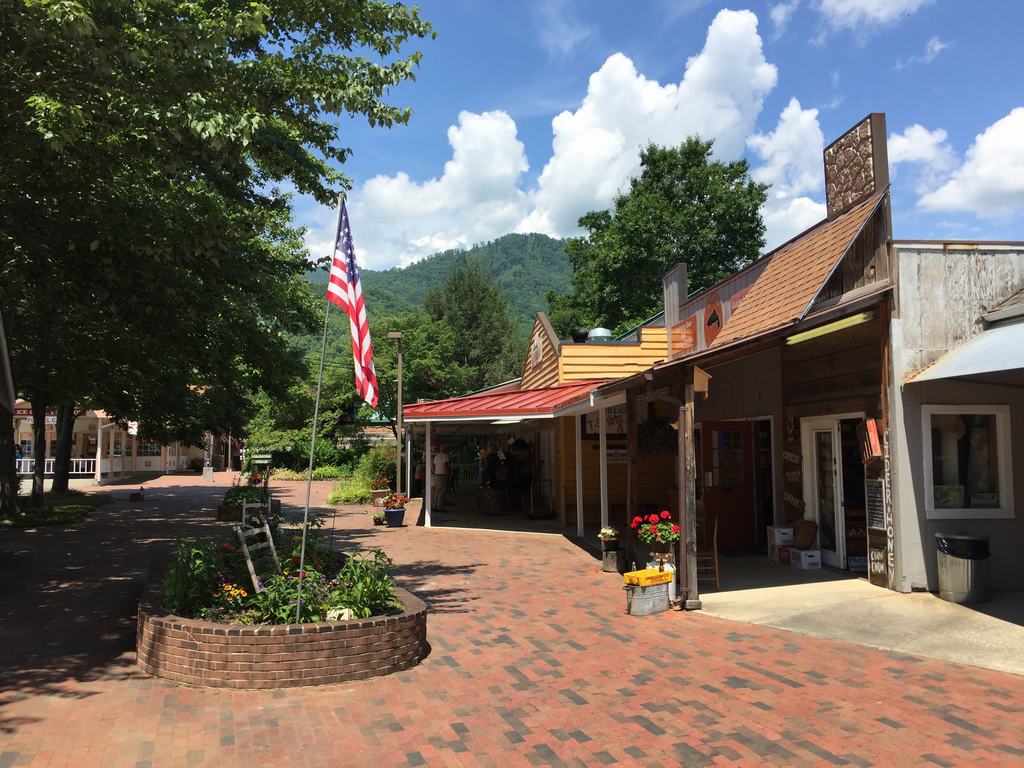 Cihlová pěší ulice s americkou vlajkou, obchody, nápis GALLERY HOME, hory