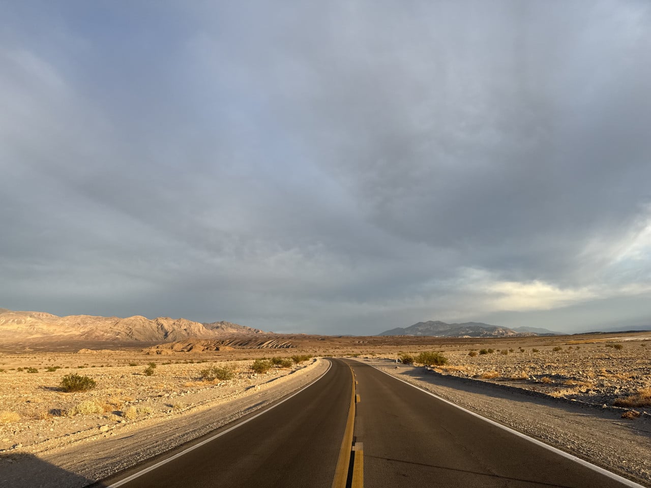 Silnice v Death Valley mezi pouštními horami pod zamračenou oblohou