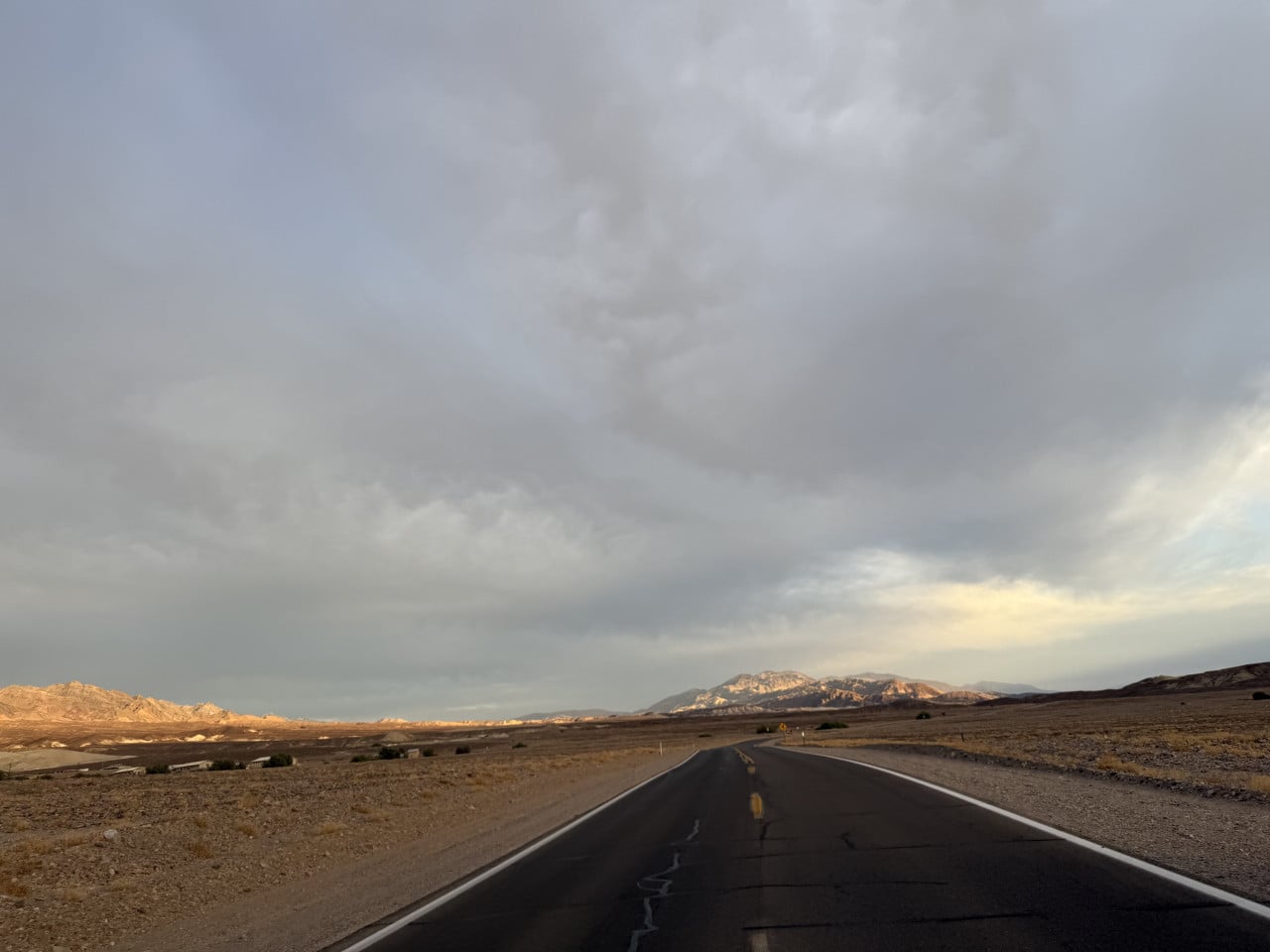 Silnice v Death Valley, pustá krajina a vzdálené hory pod zamračenou oblohou